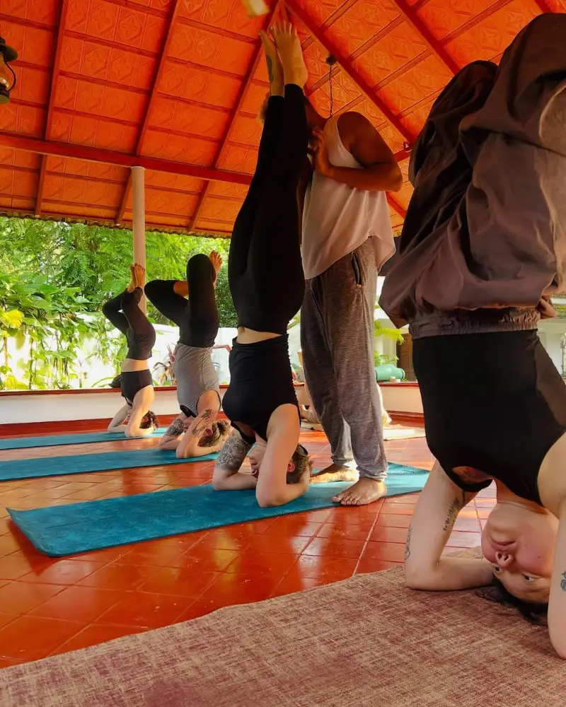 Teacher guiding a student into headstand during a class