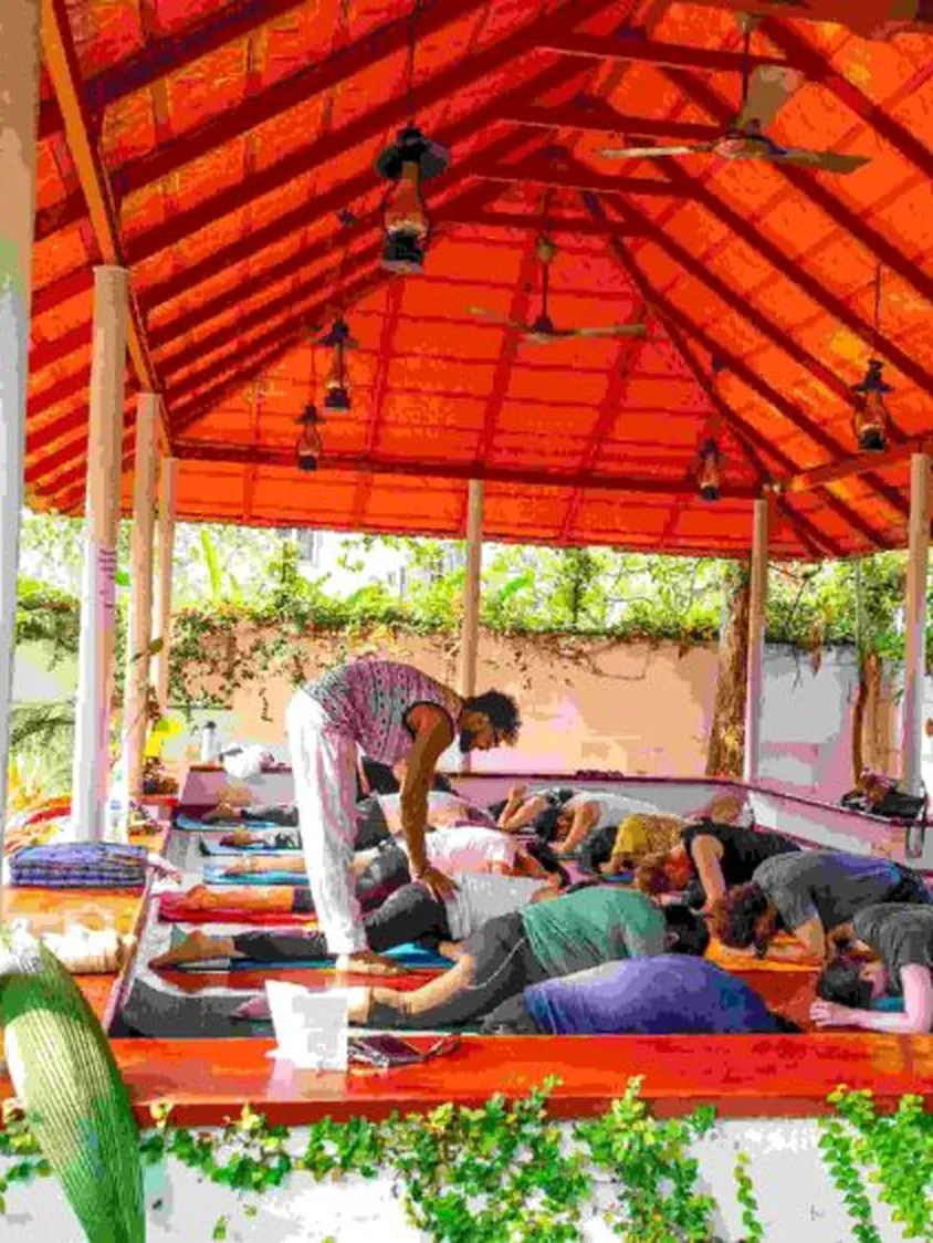 Master Aksharanand A S giving a hands-on adjustment during a class in the garden pavilion at Santhi School of Yoga and Vedanta Studies, Fort Kochi